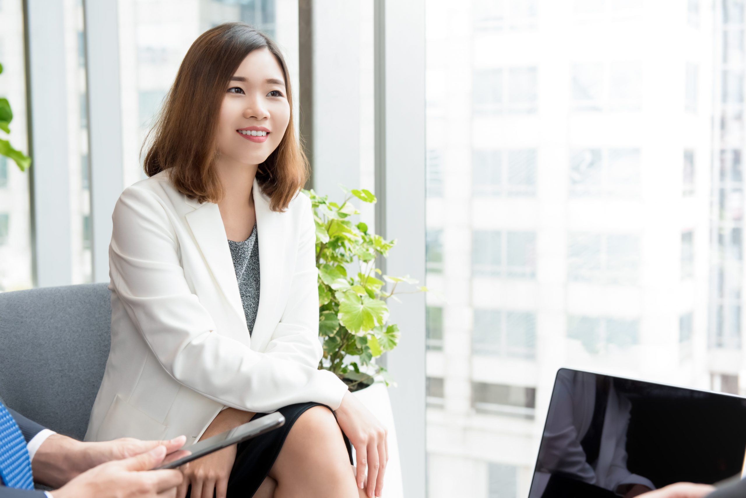 Young confident Asian businesswoman leader sitting by glass window in office lounge listening to her client in the meeting
